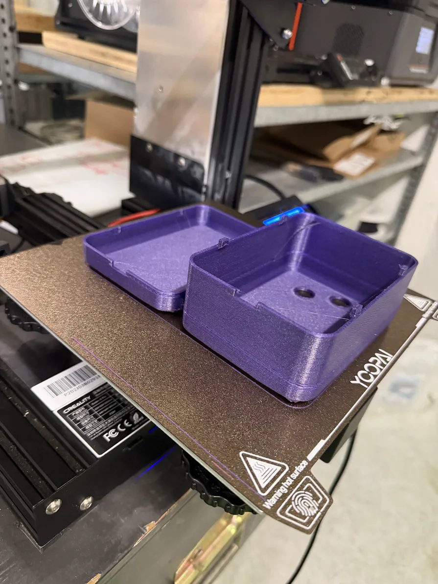 Frisch gedruckt: Ober- und Unterschale eines Controllers Zwei violette, 3D-gedruckte Gehäusehälften auf dem Druckbett eines 3D-Druckers